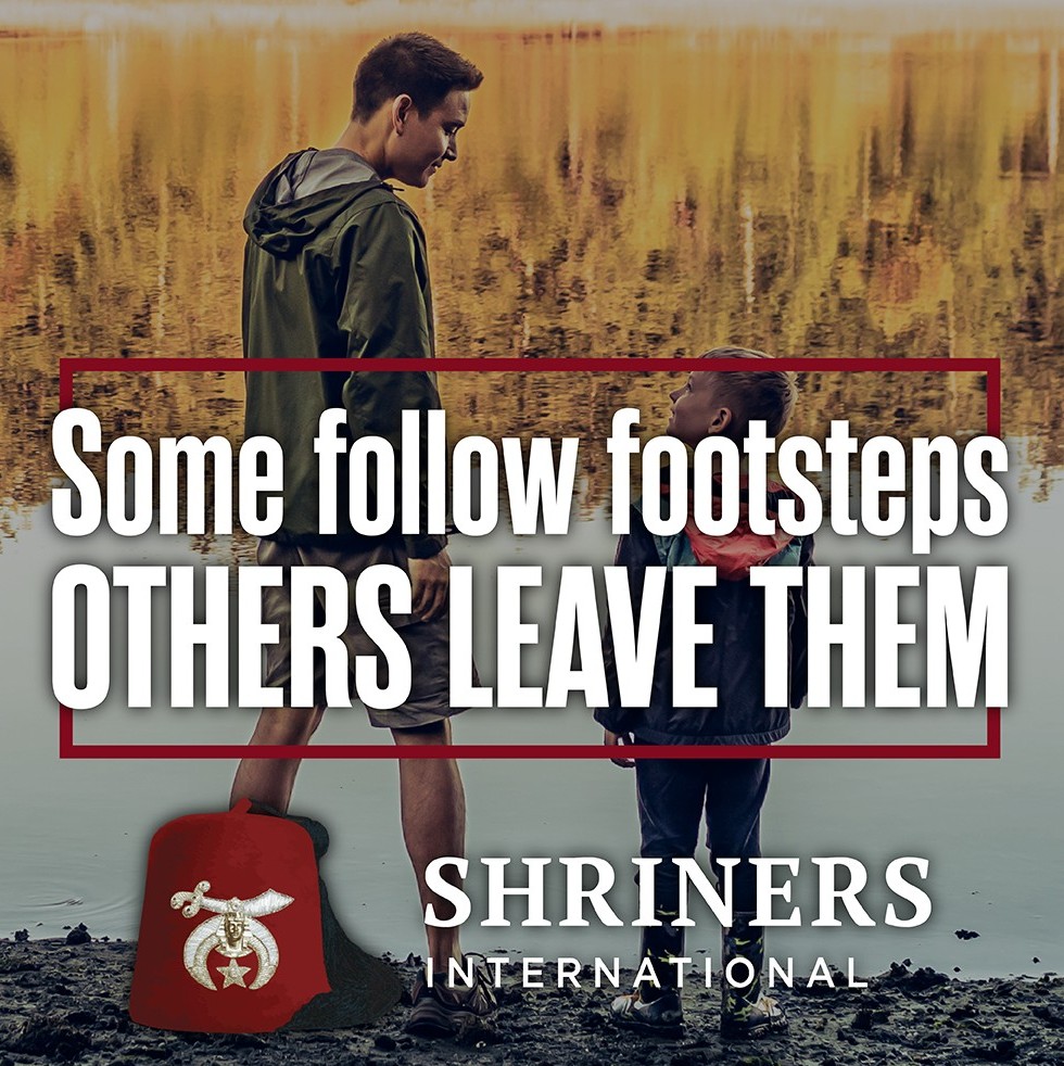 Older mentor walking beside a younger boy near a lakeshore, representing guidance and leadership, Shriners International campaign.